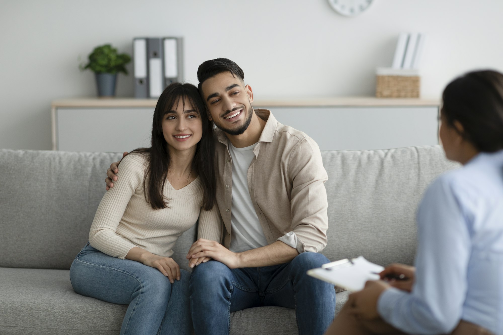 Arab married couple hugging after effective psychotherapy, spouses communicating with psychologist